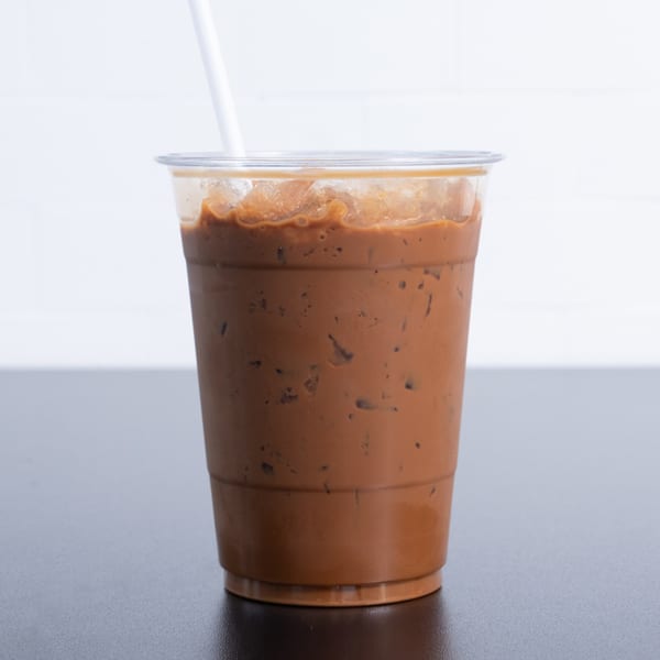 Iced Vietnamese coffee in a clear plastic cup with a white straw on a dark table.