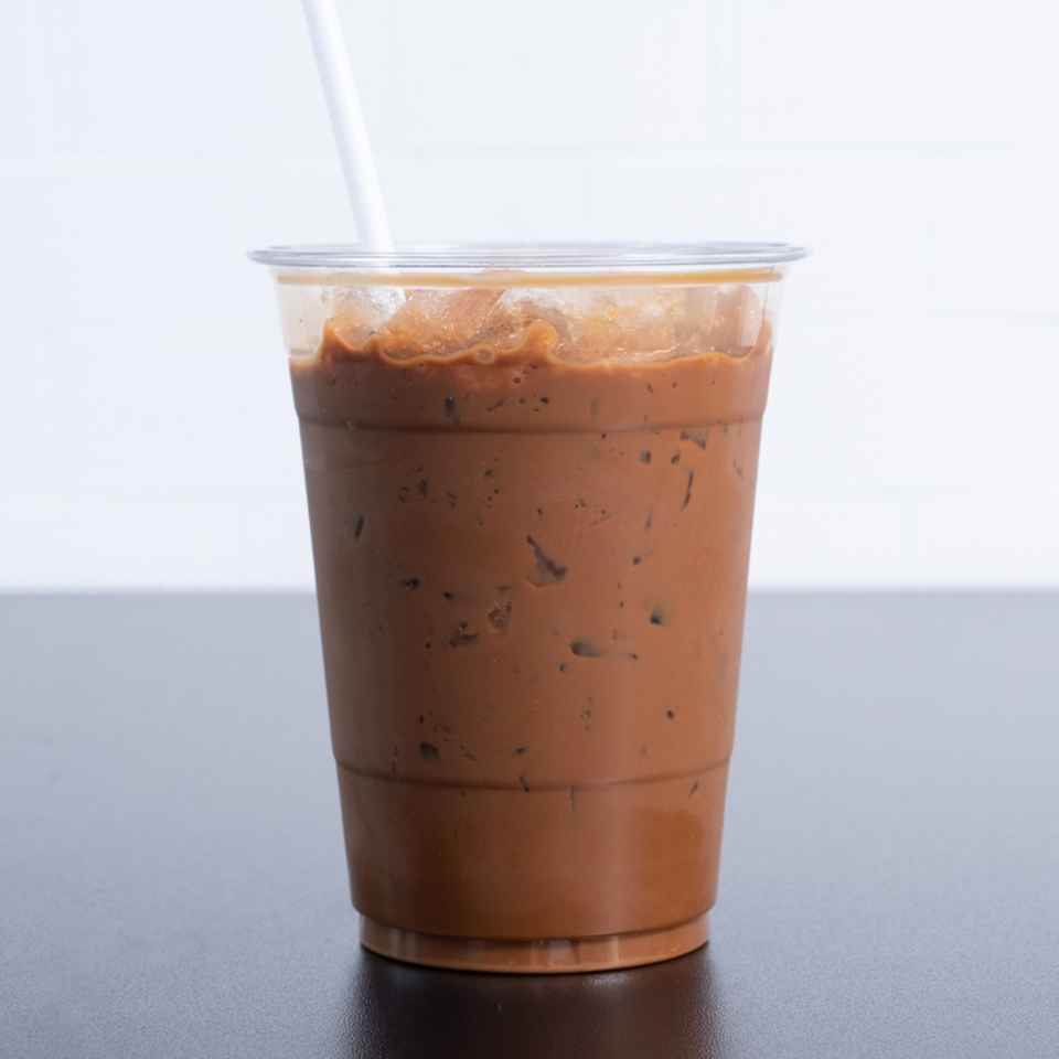 Iced Vietnamese coffee in a clear plastic cup with a white straw on a dark table.
