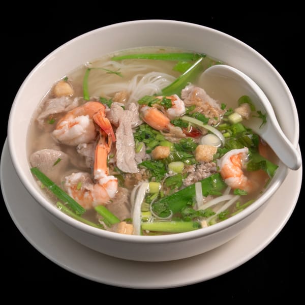A bowl of Vietnamese Phở Skyline soup with noodles, shrimp, pork, and green onions.
