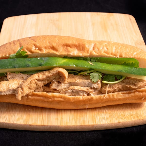 A Vietnamese Banh Mi sandwich, filled with meat, cucumber, and cilantro, on a wooden board.
