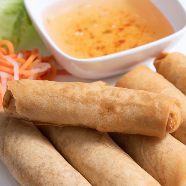 Crispy Vietnamese spring rolls with a side of dipping sauce and pickled vegetables.