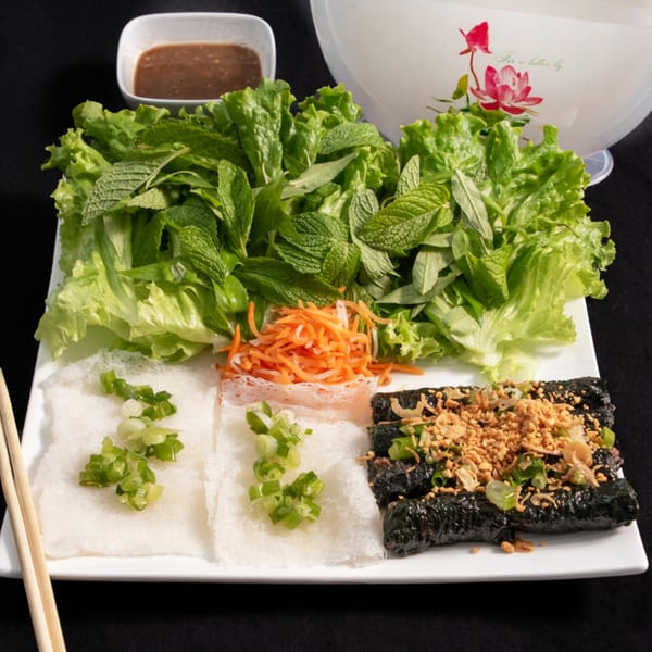 Vietnamese grilled pork sausage with fresh herbs, rice paper, pickled carrots, and dipping sauce.