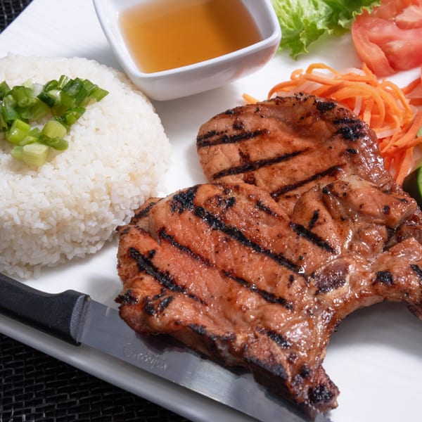 Grilled pork chops with rice, green onions, pickled carrots, and a side of dipping sauce.